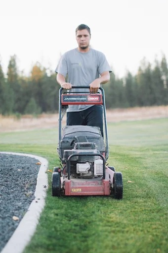 Crew member mowing a manicured lawn with a walk-behind mower